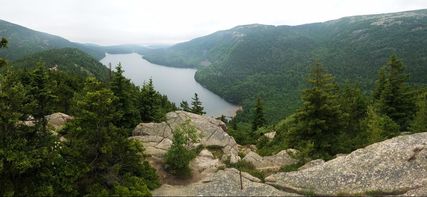 Picture: Mountain overlook from Bubbles Trail in Acadia National Park. Photo taken from a rocky outcrop and a large lake is in the background surrounded by thick forests. 
